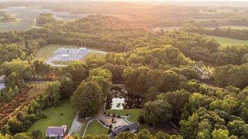 An aerial view of a rural property with a large field, a small pond, and a fenced area with a building.