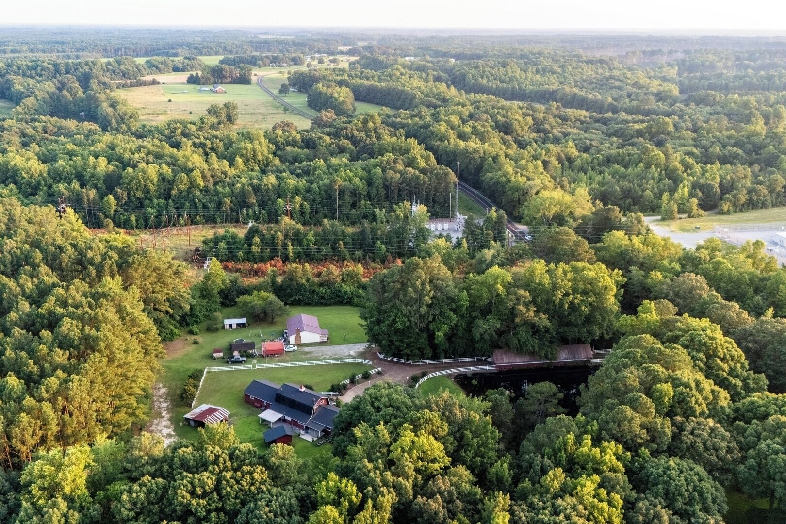 Vue aérienne d’une propriété rurale comprenant une grande maison, des granges et des zones boisées environnantes.