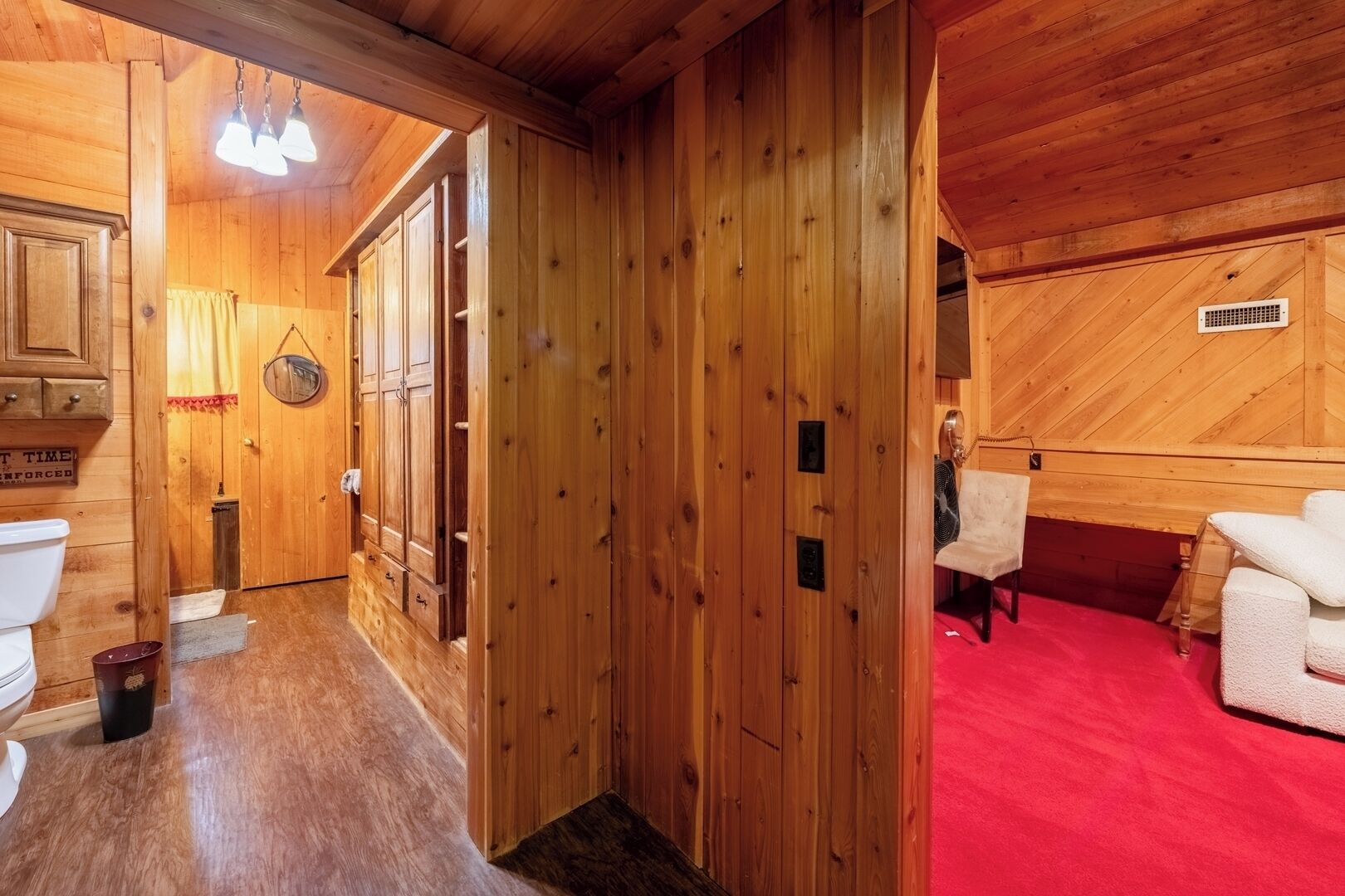 Een houten interieur met een rood tapijt, een witte stoel en een ventilator.