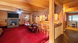 A cozy wooden cabin interior with a fireplace, leather sofa, and a bar area. - Pet-friendly 3BR Lake House Firepit & Pier (Skippers)