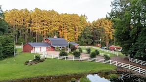 A red barn with a white fence, a pond, and a forest in the background. - Pet-friendly 3BR Lake House Firepit & Pier (Skippers)