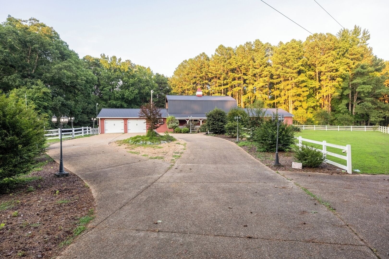 A rural property with a barn, fenced areas, and a driveway leading to a building with a red roof.