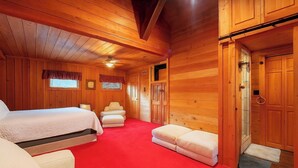 A wooden cabin bedroom with a large bed, a chair, a bench, and a door. - Pet-friendly 3BR Lake House Firepit & Pier (Skippers)