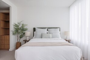 Un dormitorio con cama, dos mesitas de noche, lámpara, planta y armario de madera.
