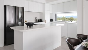 Une cuisine moderne dotée d’un îlot central, d’appareils électroménagers en acier inoxydable et offrant une vue sur l’extérieur.