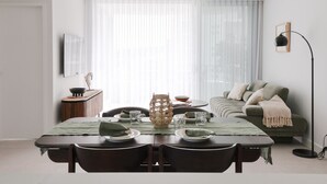 Un salon moderne avec une table à manger pour quatre personnes, un canapé, une lampe sur pied et une grande fenêtre ornée de rideaux légers.