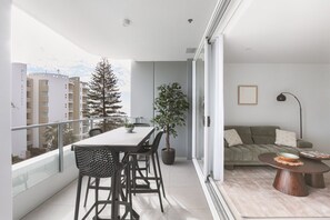 Un balcón con una mesa de comedor y sillas, una planta en maceta y un sofá con una mesita de centro.