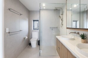 Un baño moderno con ducha envuelta en vidrio, inodoro y lavamanos con espejo superior.