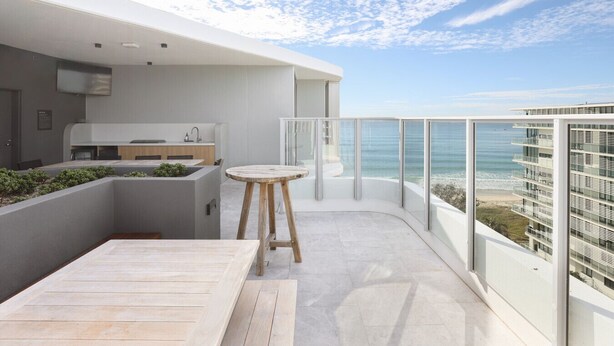 Un balcon moderne avec une table et des chaises en bois, un coin cuisine et une vue sur l’océan.