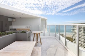A modern balcony with a wooden table and chairs, a kitchen area, and a view of the ocean. - The Sunstream Haven Palm Beach (Palm Beach)