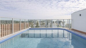 Une piscine sur le toit, avec une eau d’un bleu cristallin, entourée de rampes de verre et offrant une vue sur le paysage urbain.
