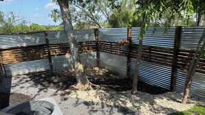 Un espacio al aire libre cercado con suelo de grava, un banco de madera y un ventilador pequeño.