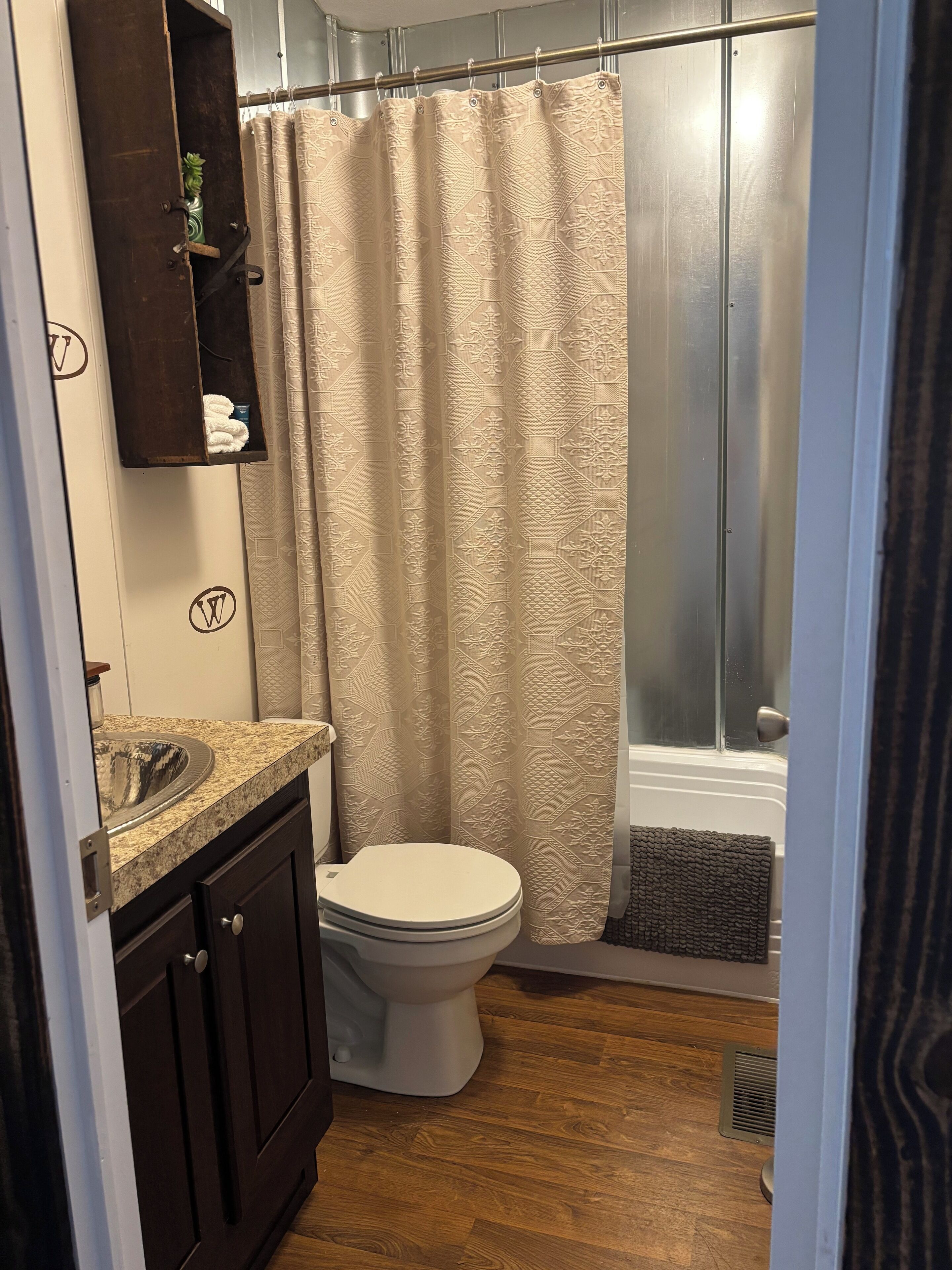 A bathroom with a toilet, a sink, a shower curtain, and a wooden floor.