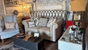 Una sala de estar acogedora con un estilo vintage, que incluye un sofá capitonado, un sillón clásico y una mesa de centro de madera.