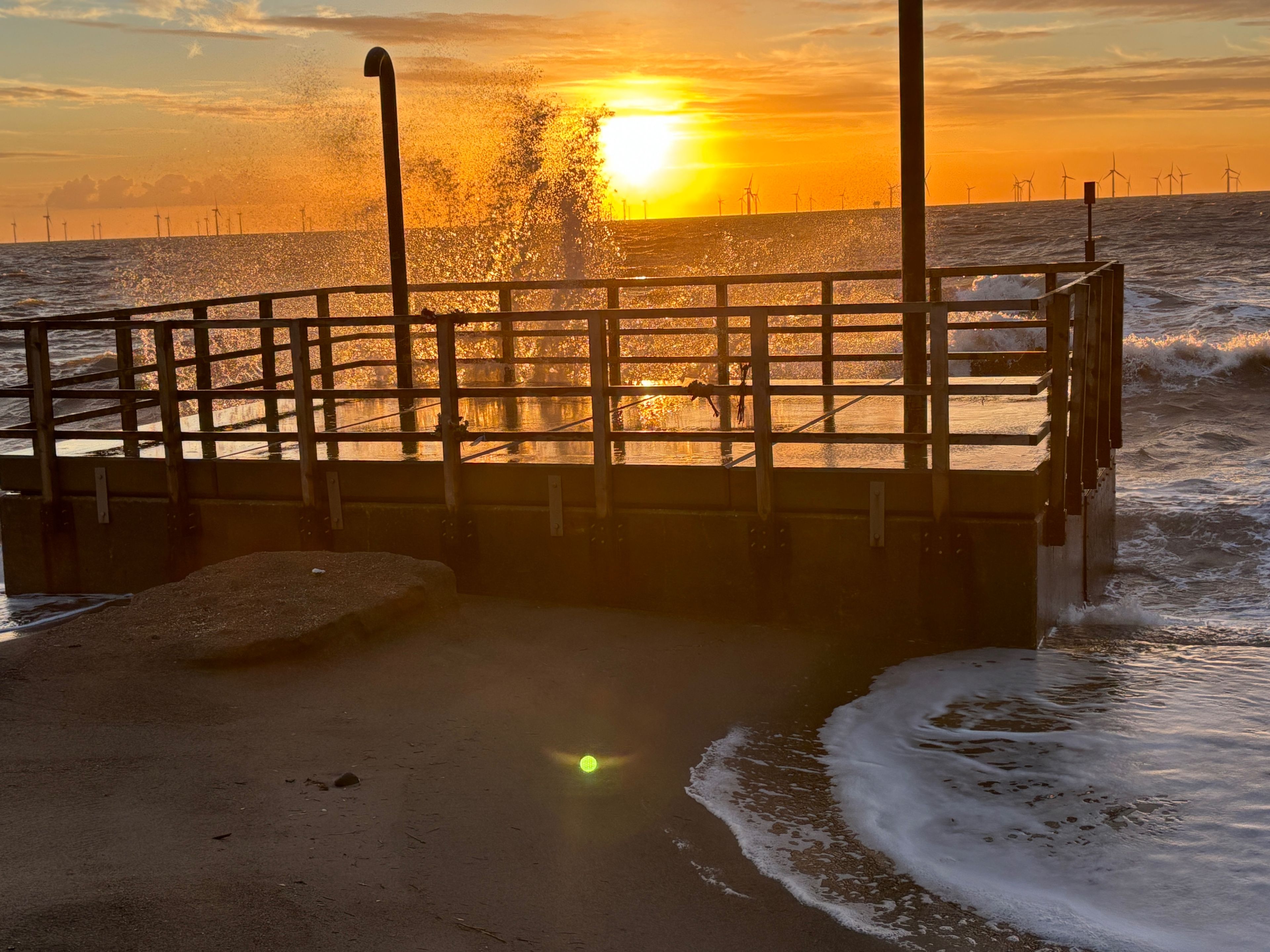 A wooden pier extending over a sandy beach with waves crashing below, leading to a body of water.