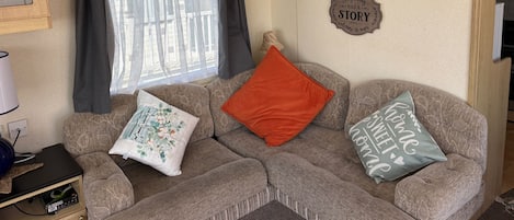 A cozy living room with a sofa, decorative pillows, a wall clock, and a window with curtains.
