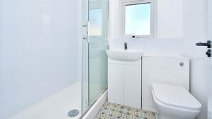 Kylpyhuone, jossa on lasinen suihkuseinä, valkoinen pesuallas ja wc.