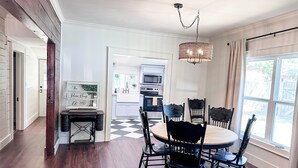 A dining area with a round table and chairs, a chandelier, and a view of the kitchen in the background. - The Pecan Street Retreat - 1935 Gem (Searcy)