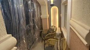 A narrow hallway with a covered outdoor area, wicker chairs, a table, and a pendant light.