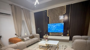 A modern living room with a sectional sofa, a coffee table, and a flat-screen TV mounted on the wall.