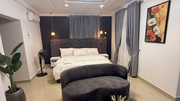 A modern bedroom with a curved bed, a round coffee table, and a large potted plant.