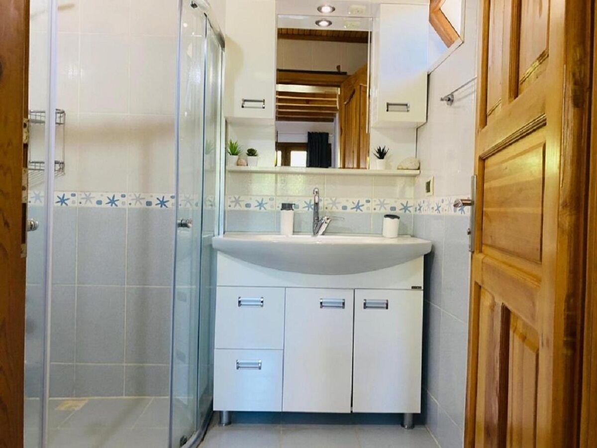 A bathroom with a glass shower enclosure, a white sink with a mirror above it, and wooden doors.