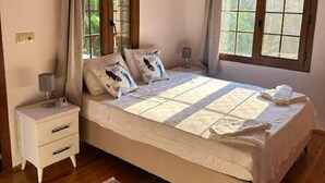 A bedroom with a wooden ceiling, a bed with a quilt, two bedside tables, a nightstand, a window with curtains, and a patterned rug. - Spacious Stone Villa in the heart of Kayakoy, Overlooking the historic ruins. (Fethiye)