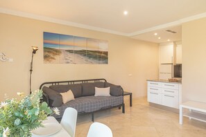 A modern living room with a sofa, a dining table, and a kitchen area.