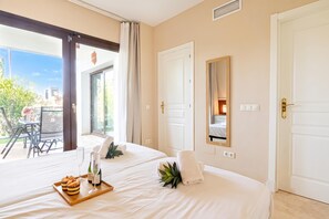 A hotel room with two beds, a dining area with a table and chairs, and a large window with a view of the outdoors.