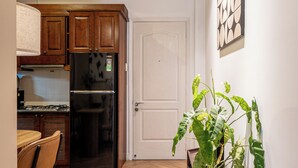 A compact kitchen with wooden cabinets, a black refrigerator, and a dining area with a chair.