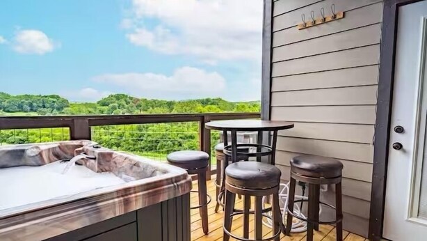 A hot tub area with a wooden deck, a round table, and two barstools. - Modern•Prime Location•Mountain Views•Theater•Hot Tub•minutes to ALL attractions! (Sevierville)