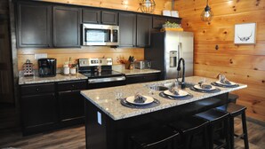 A modern kitchen with dark cabinets, granite countertops, stainless steel appliances, and a central island with bar stools. - Modern•Prime Location•Mountain Views•Theater•Hot Tub•minutes to ALL attractions! (Sevierville)