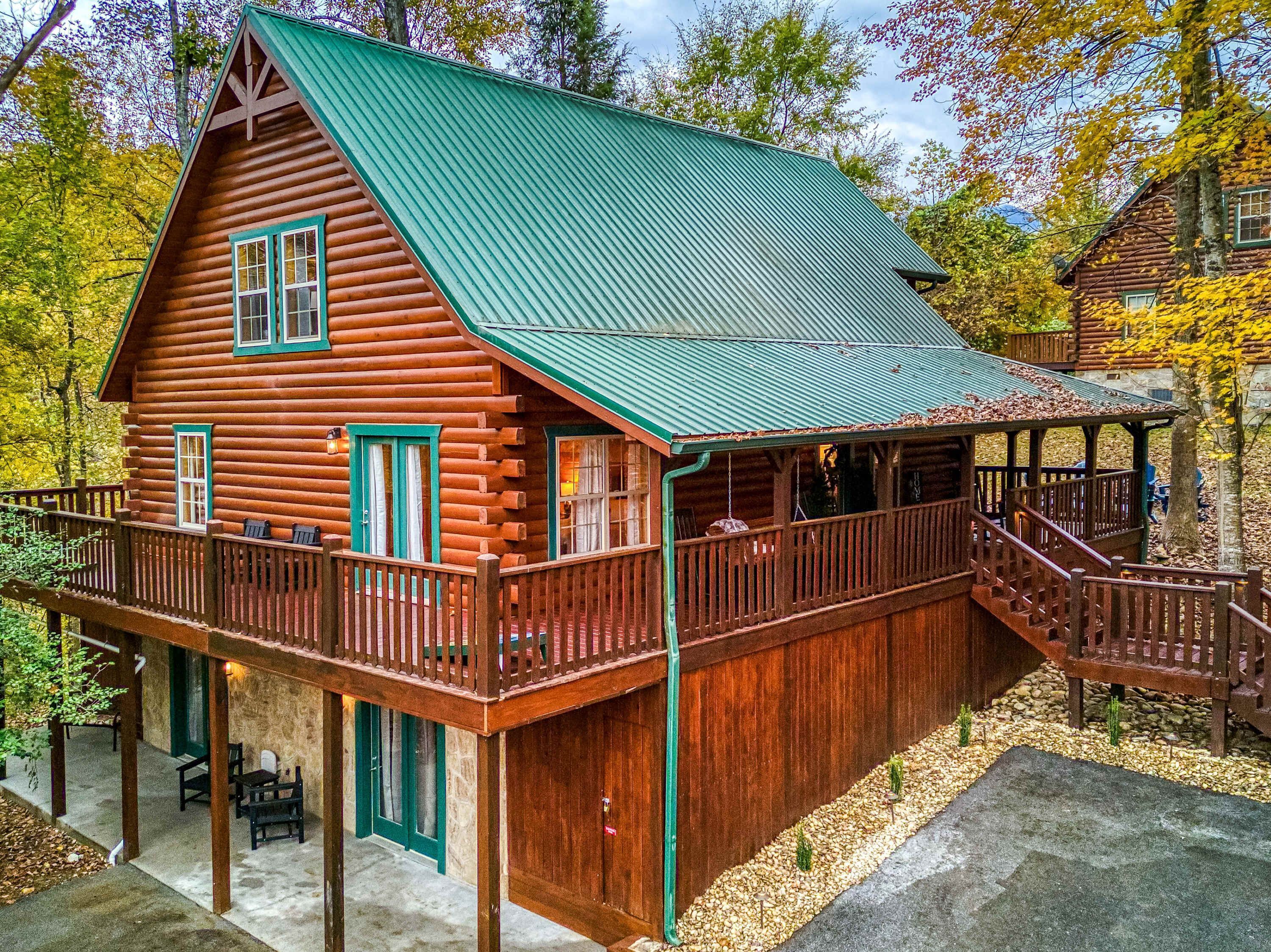 A log cabin with a green metal roof, a balcony, and a covered porch.