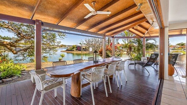 An outdoor dining area with a wooden table and chairs, overlooking a body of water and a pool. - Maroochydore Waterfront (Maroochydore)