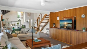 A modern living room with a wooden accent wall, a large flat-screen TV, a staircase, and a cozy seating area with a sofa and coffee table. - Maroochydore Waterfront (Maroochydore)