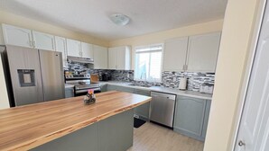 A modern kitchen with grey cabinets, a wooden countertop, stainless steel appliances, and a window providing natural light. - Whole House to Yourself! Cozy Suburban Getaway Near Riverside Pathways  (Calgary)