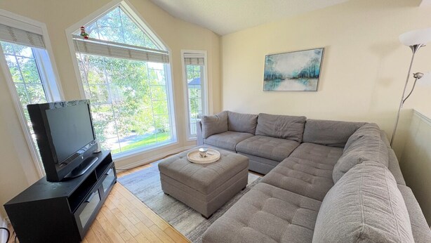 A living room with a large sectional sofa, a flat-screen TV on a black stand, and a painting on the wall. - Whole House to Yourself! Cozy Suburban Getaway Near Riverside Pathways  (Calgary)