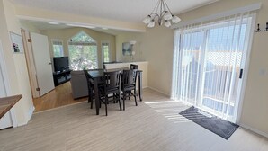 A spacious living room with a dining area, a kitchen in the background, and a sliding glass door leading to a balcony. - Whole House to Yourself! Cozy Suburban Getaway Near Riverside Pathways  (Calgary)