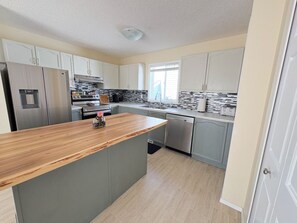 A modern kitchen with grey cabinets, a wooden countertop, stainless steel appliances, and a window providing natural light.