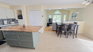 A spacious kitchen with a wooden island, a dining area with dark chairs, and a view through a large window. - Whole House to Yourself! Cozy Suburban Getaway Near Riverside Pathways  (Calgary)