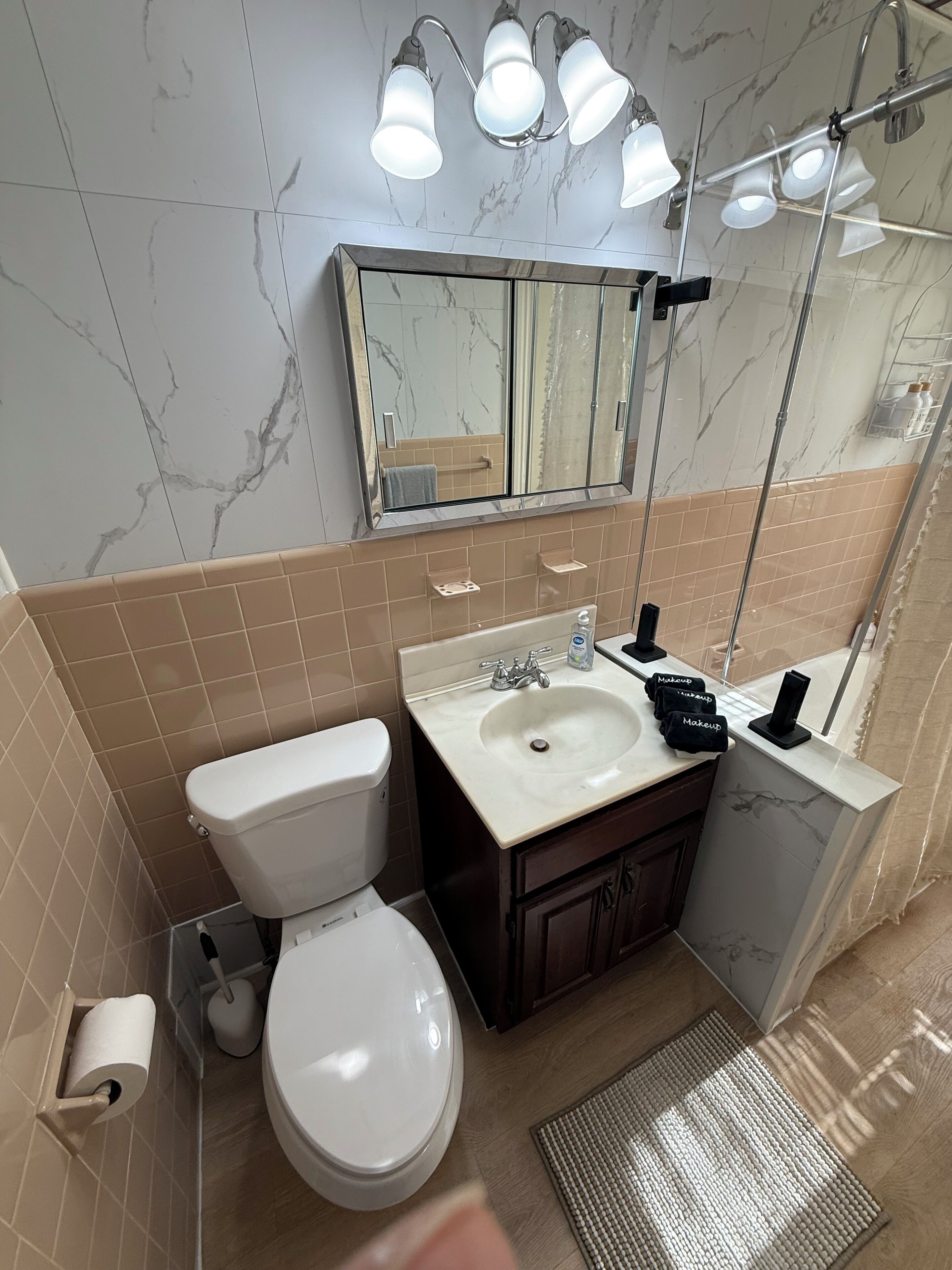 A bathroom with a toilet, sink, mirror, and shower.