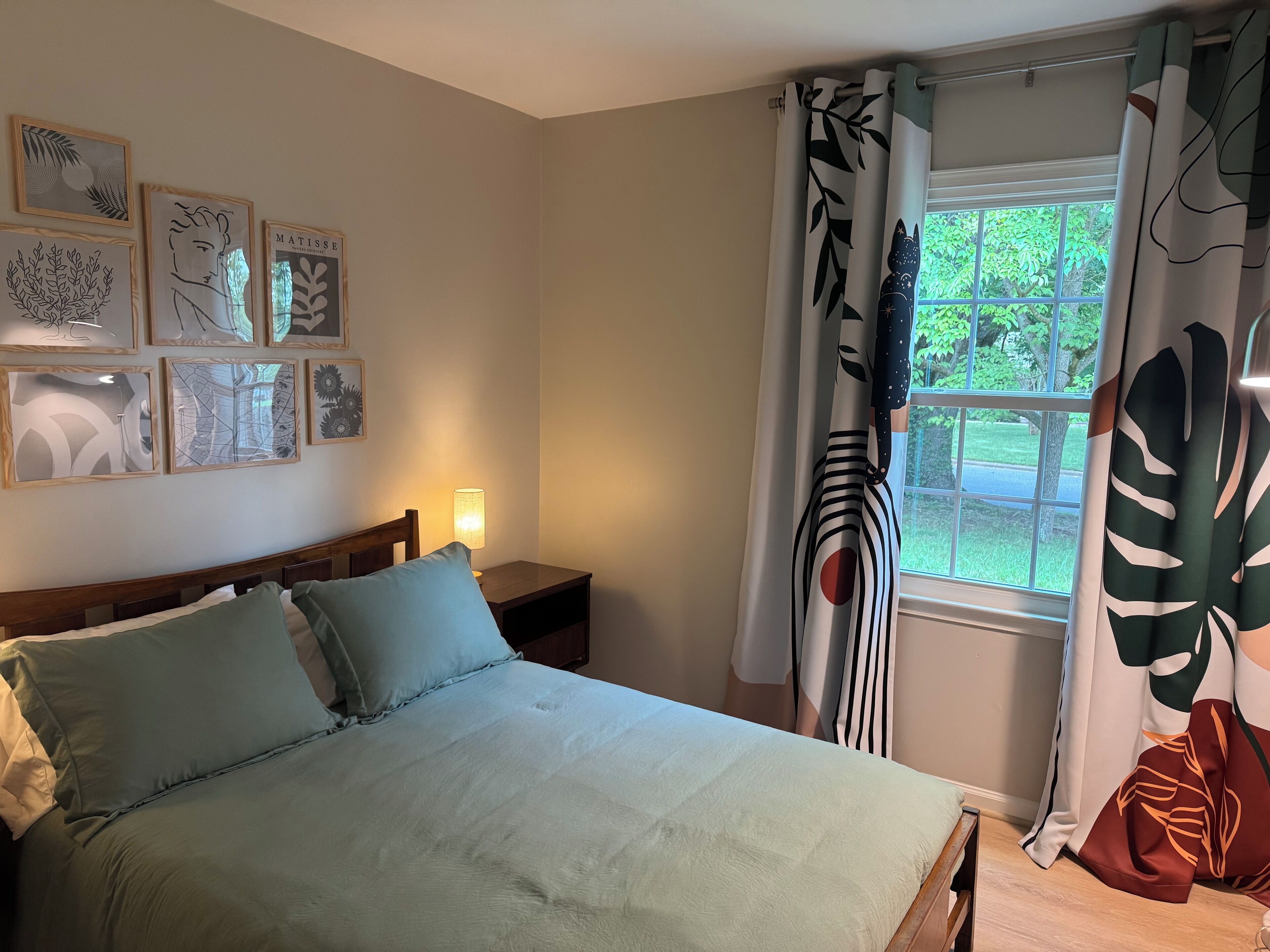 A bedroom with a bed, a nightstand, a lamp, and a window with curtains.