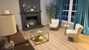 A living room with a fireplace, two armchairs, a coffee table, and a lamp. - Chic 3 Bedroom Midcentury Modern Retreat in Wonderful Greensboro (Greensboro)