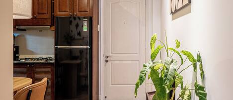 A compact kitchen with wooden cabinets, a black refrigerator, and a dining area with a chair.