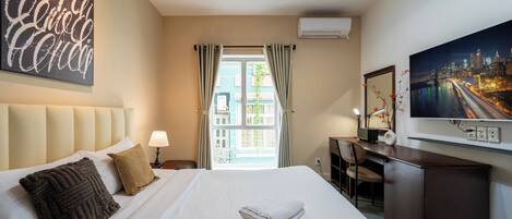 Una habitación de hotel con cama, escritorio, silla, televisor y ventana con cortinas.