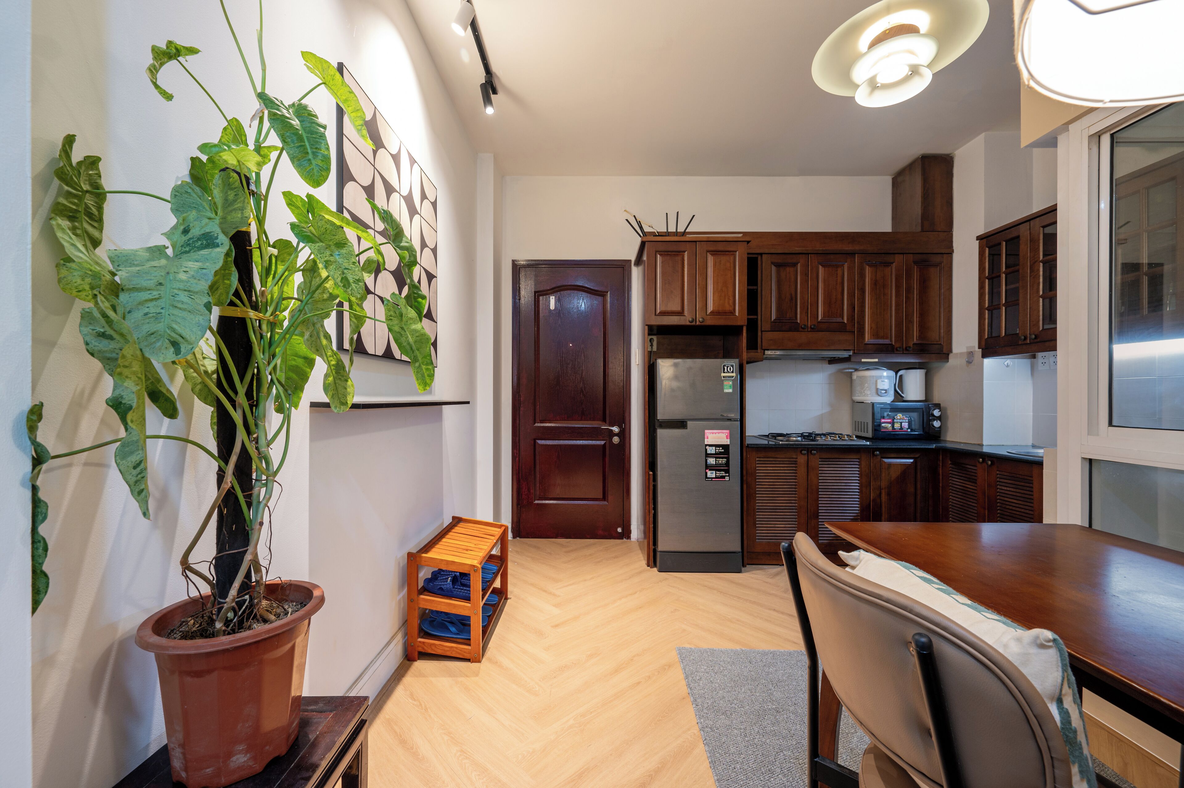 Une cuisine de taille réduite, avec des meubles de rangement en bois, un réfrigérateur et une plante en pot.