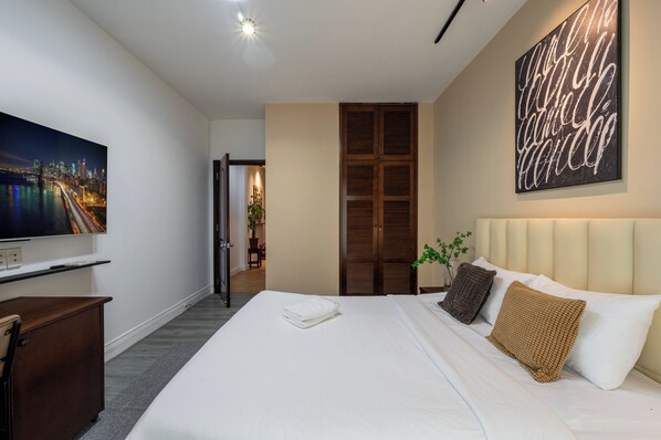 A modern hotel room with a large bed, a flat-screen TV, a wooden wardrobe, and a cityscape painting on the wall.