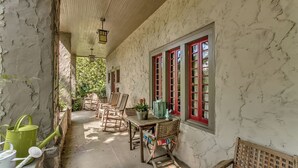 A covered outdoor area with stone walls, red-framed windows, and wooden furniture.