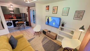 Ein modernes Wohnzimmer mit Sofa, Fernseher, Essbereich und Küche.