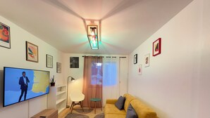 Ein modernes Wohnzimmer mit Flachbildfernseher, einem gelben Sofa, einem weißen Sessel und einem kleinen Tisch.